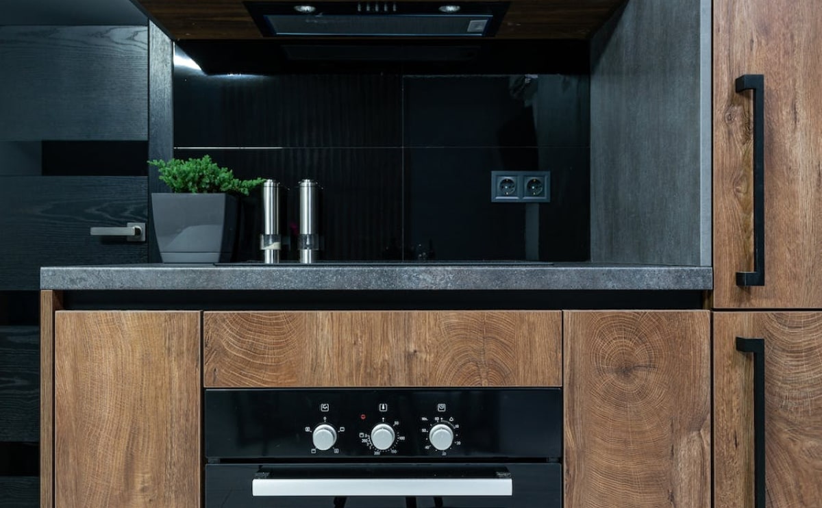 Modern kitchen with black backsplash, wood-grain cabinets, and sleek black appliances accented by minimalist décor.